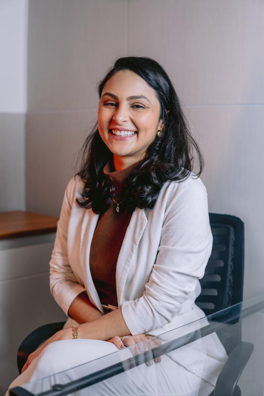 Chyuiene rindo, sentada no consultório, de blazer branco.